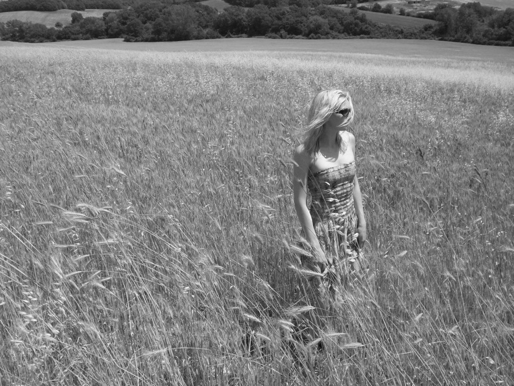 A woman stands in a lush, grassy field, her hair gently blowing in the wind, capturing a serene moment in nature.